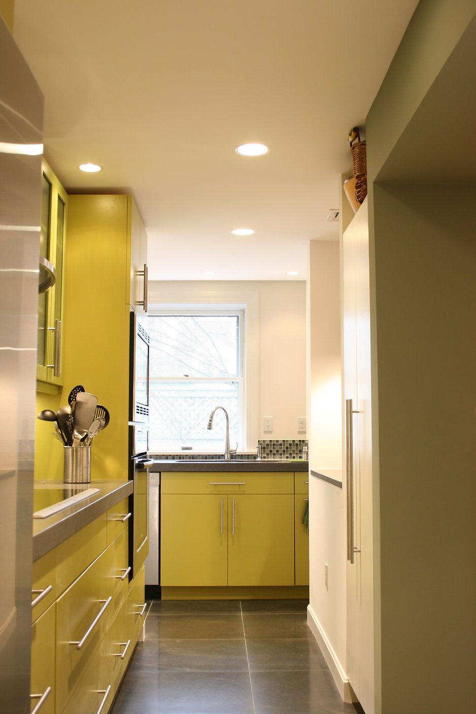 Narrow kitchen with yellow cabinets, stainless steel appliances, and a window at the end.