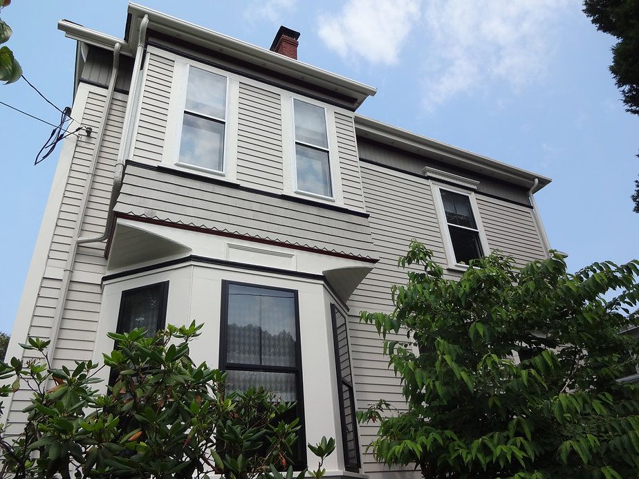 Two-story Victorian house with gray siding, dark window frames, and a partial bay window.