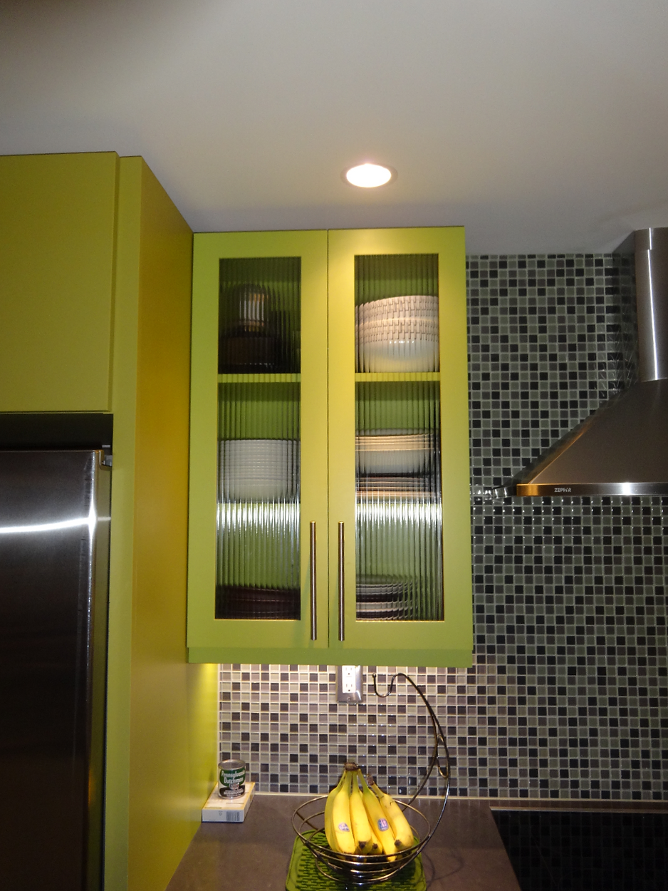 Lime green kitchen cabinets with glass doors, displaying dishes, over a mosaic backsplash.