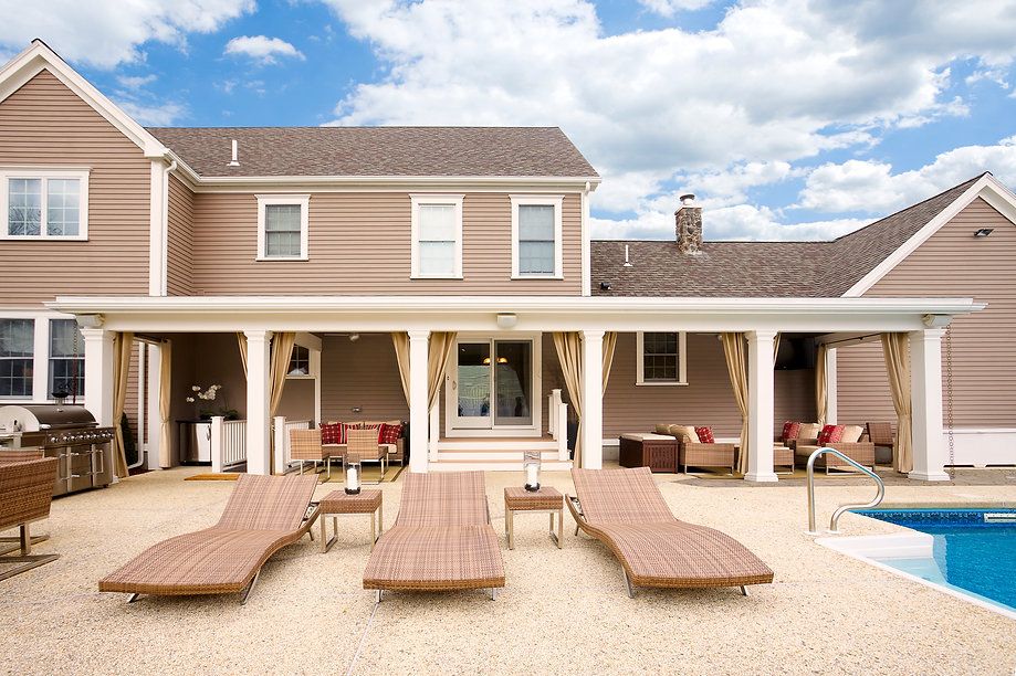 Backyard with pool, house, and covered patio with seating and lounge chairs.