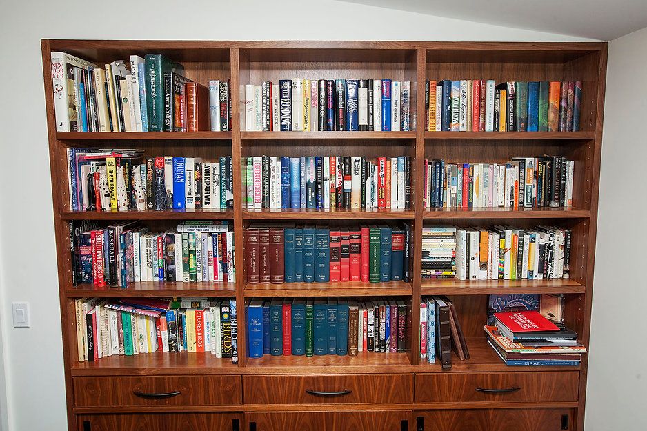 Wooden bookshelf filled with books. Brown wood, three shelves, drawers below.