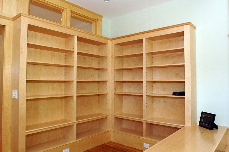 Built-in wooden bookshelves in a corner, shelves are empty. Light wood and light green walls.