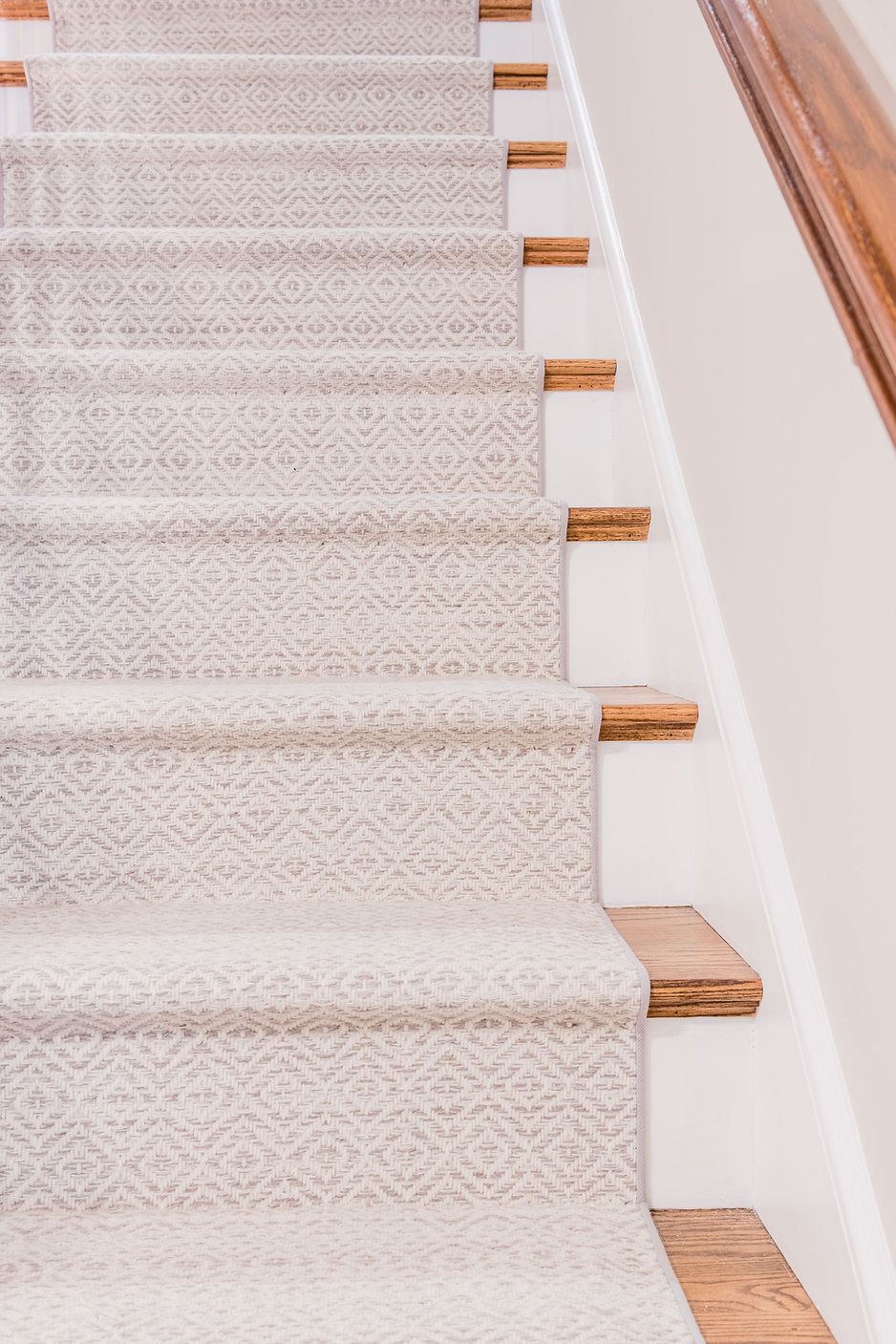 Carpeted stairs with wood treads and a white wall.