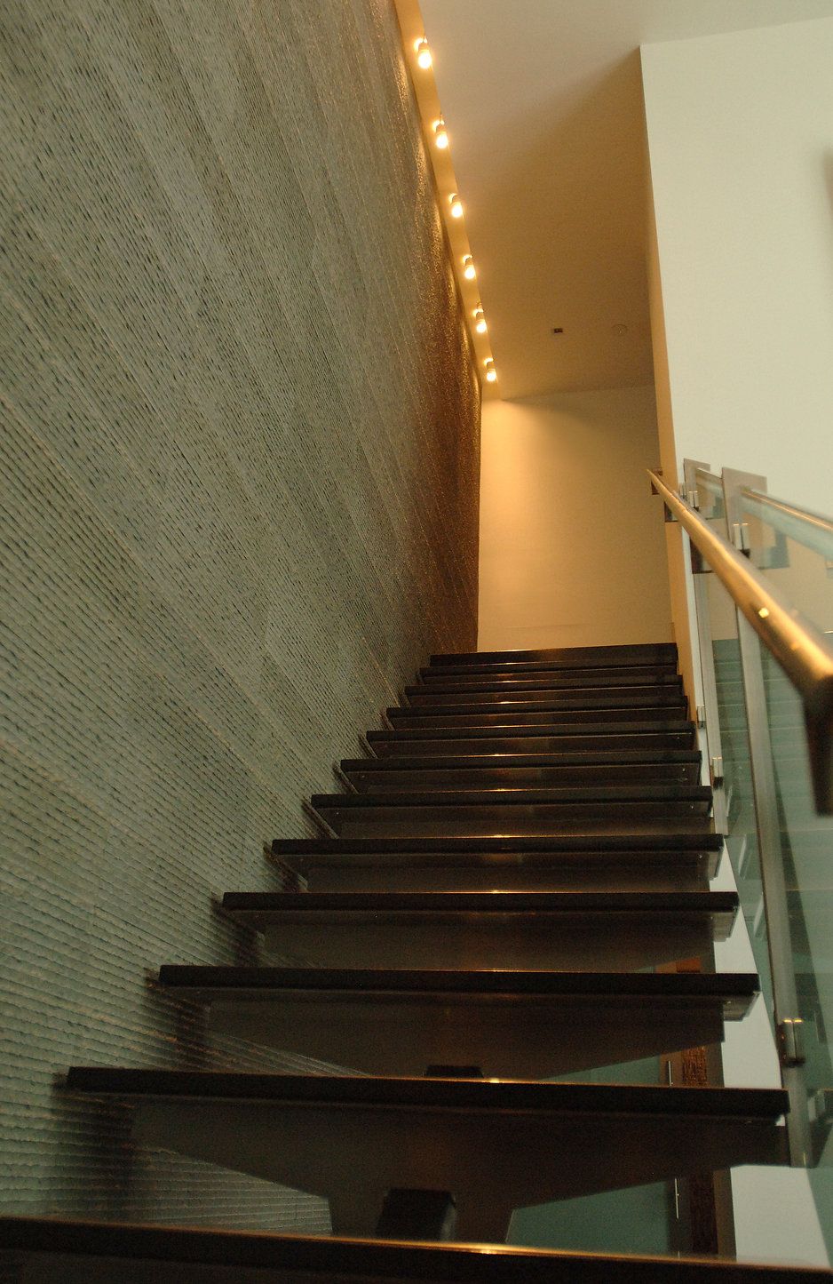 Staircase ascending, with dark wood steps, textured wall, and glass railing.