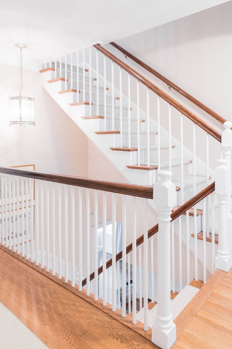 Staircase with white banisters, brown handrails and steps. Located in a light-filled hallway.