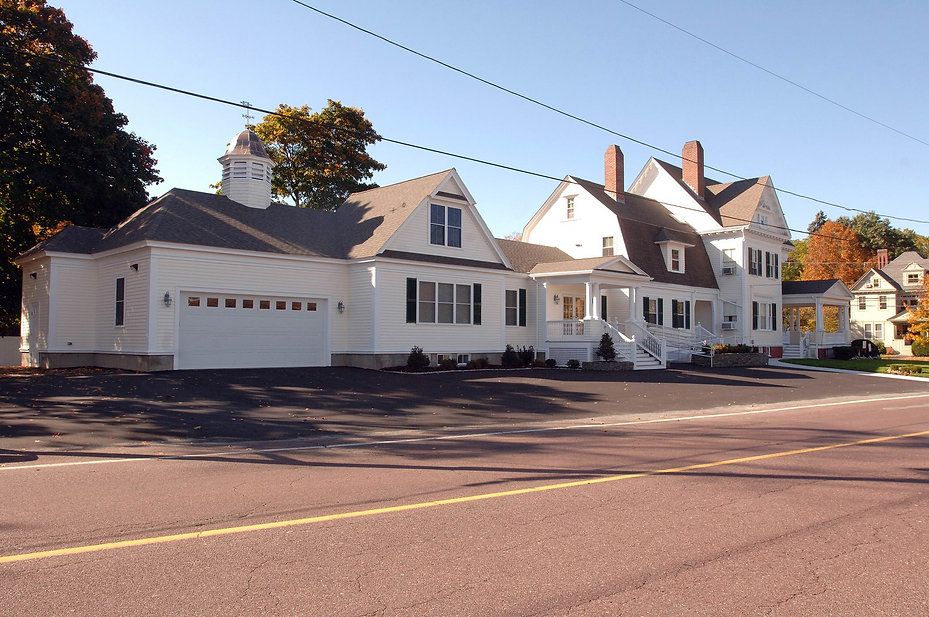 White house with a garage, porch, and multiple gabled roofs, set against a blue sky.
