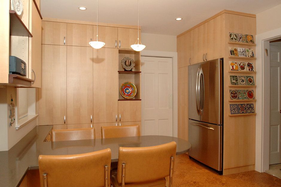 Modern kitchen with blonde cabinets, stainless steel fridge, and table with chairs.