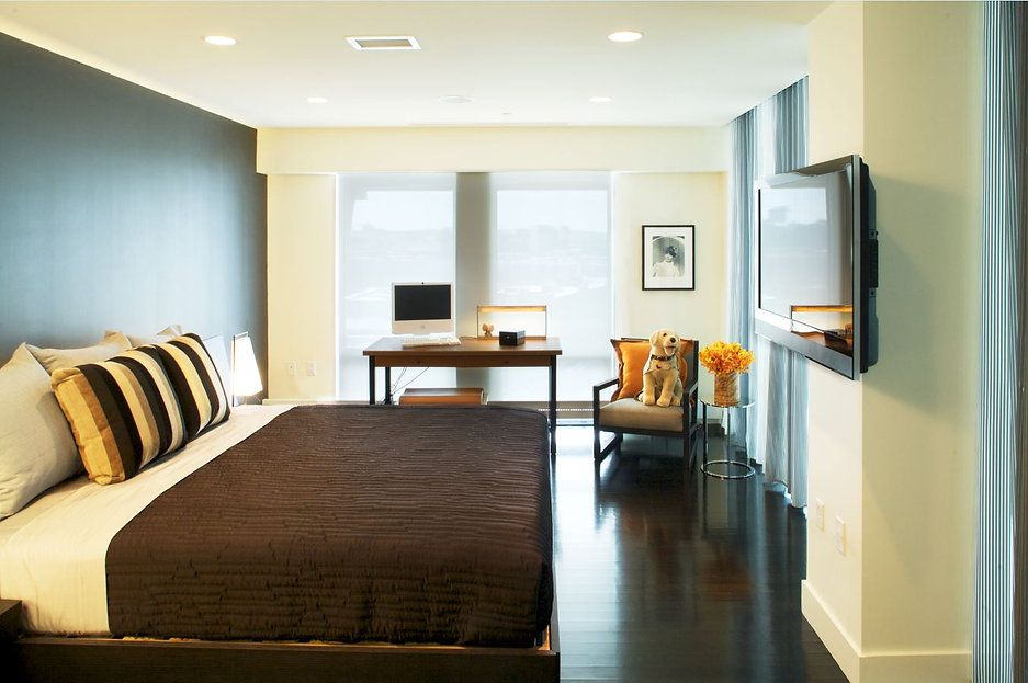 Bedroom with dark walls, bed, desk, chair, and TV. Black floor, white trim, and large windows.