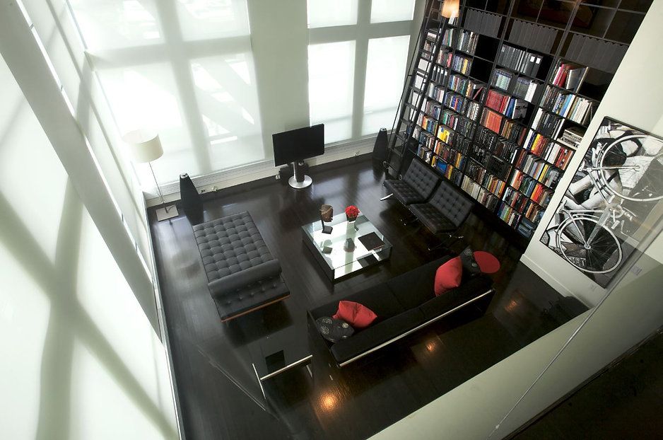Modern living room, high angle view. Black furniture, large bookshelf, tall windows, art on wall.