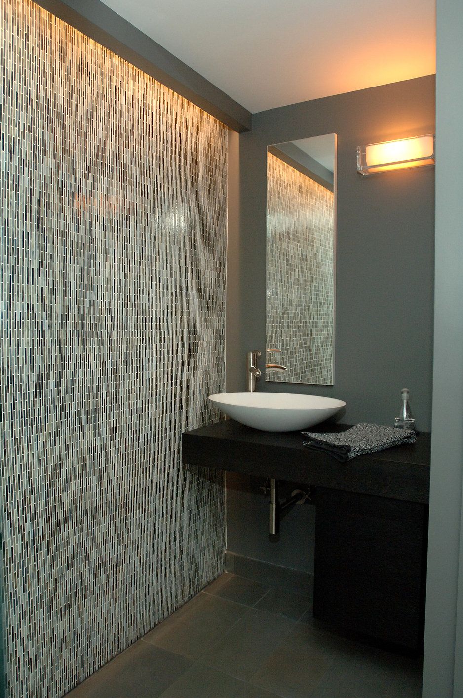 Modern bathroom with textured wall, vessel sink, dark vanity, and mirror.