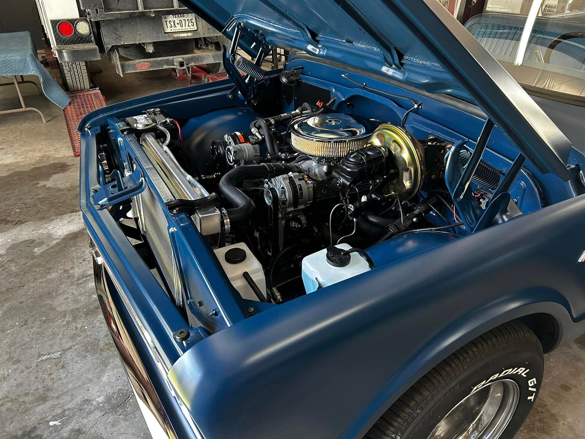 Blue classic pickup truck engine bay, hood open, showing engine components and chrome.