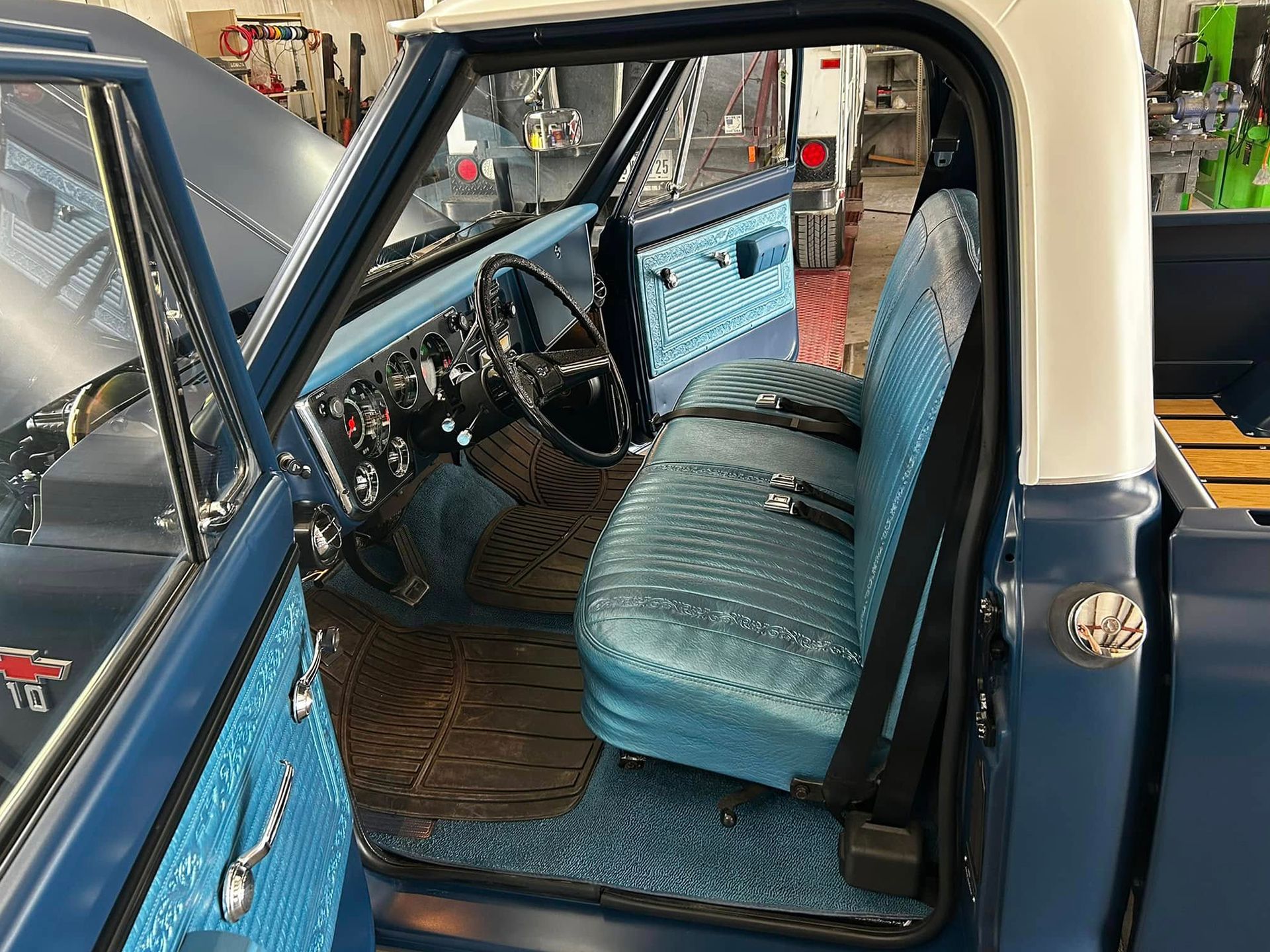 Blue vintage truck interior with blue seat, dashboard, and trim. Driver's side door is open.