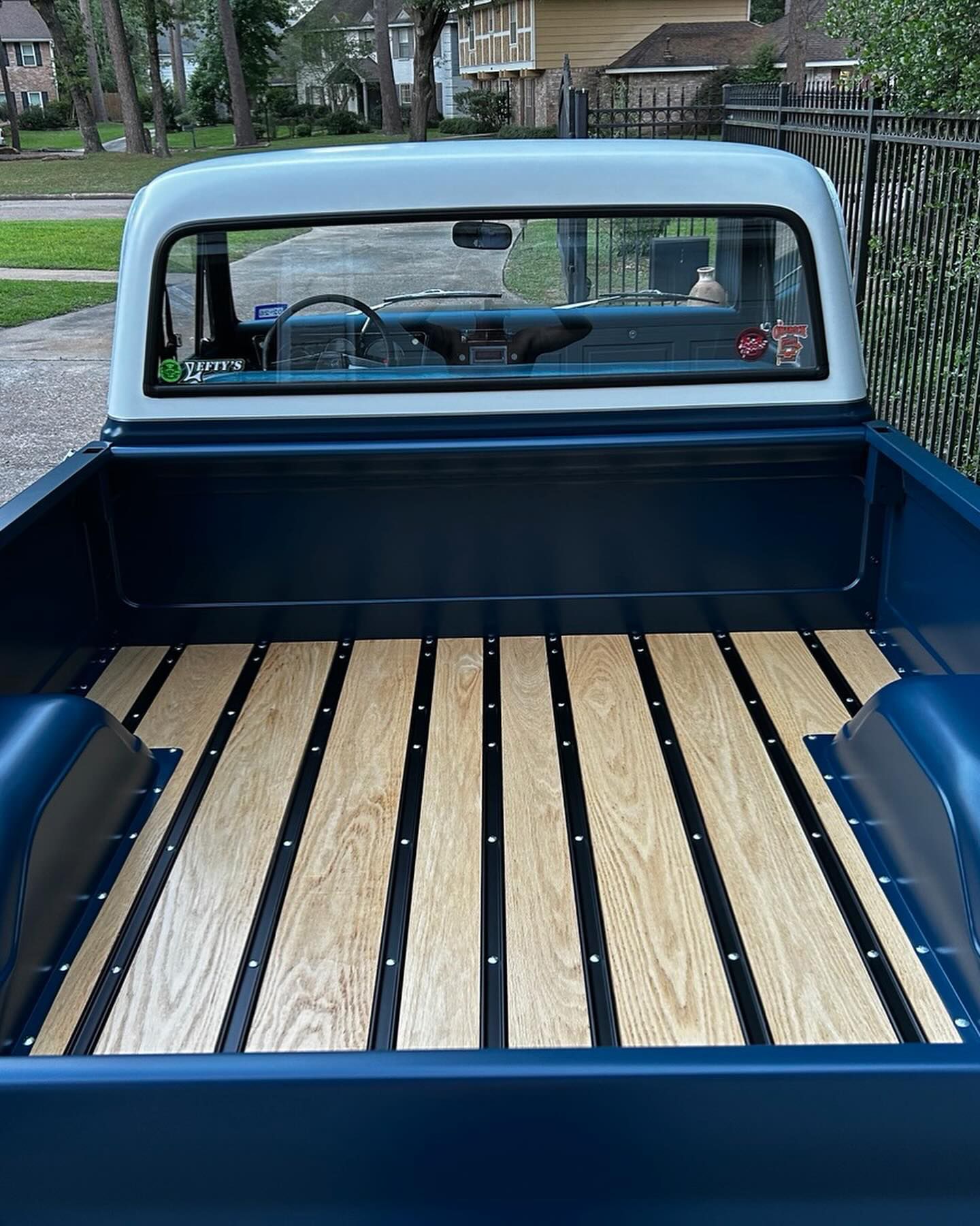 Blue classic pickup truck bed with wooden floor, white cab.