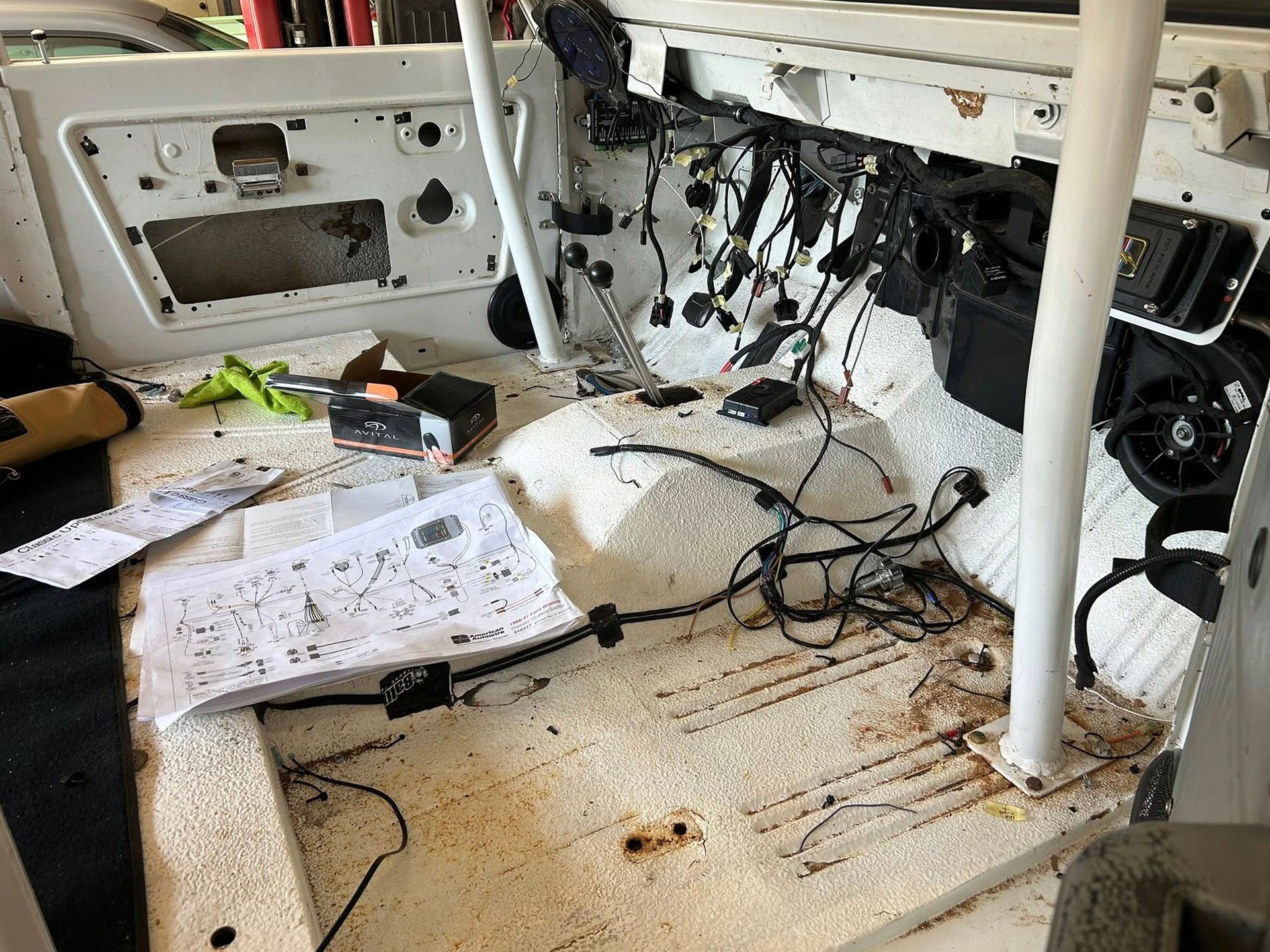 Interior view of a white vehicle, with wiring and components exposed, papers and tools on the floor.