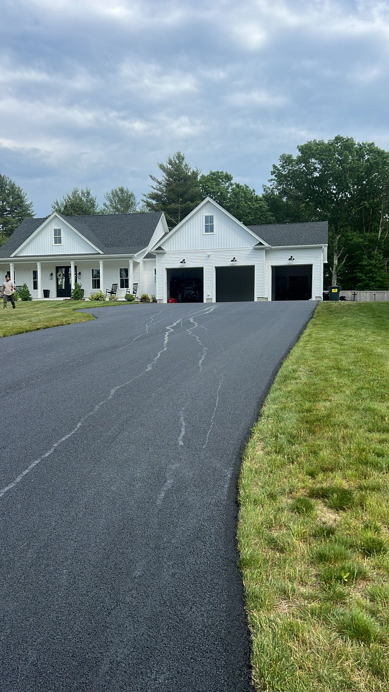 A driveway leading to a large white house with three garages.