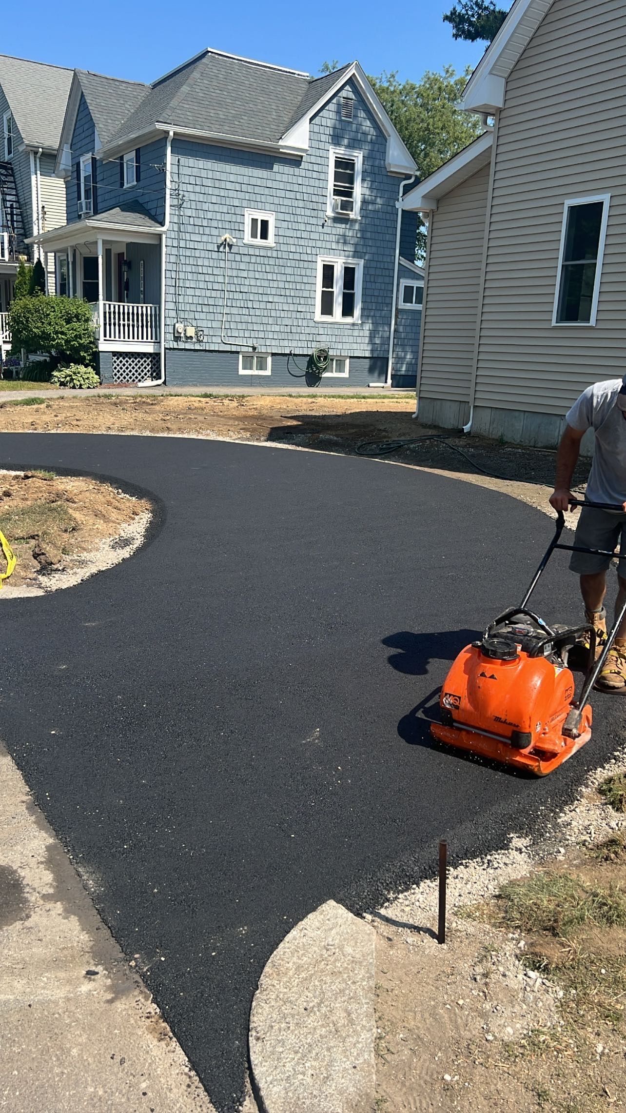 A man is paving a driveway in front of a house.