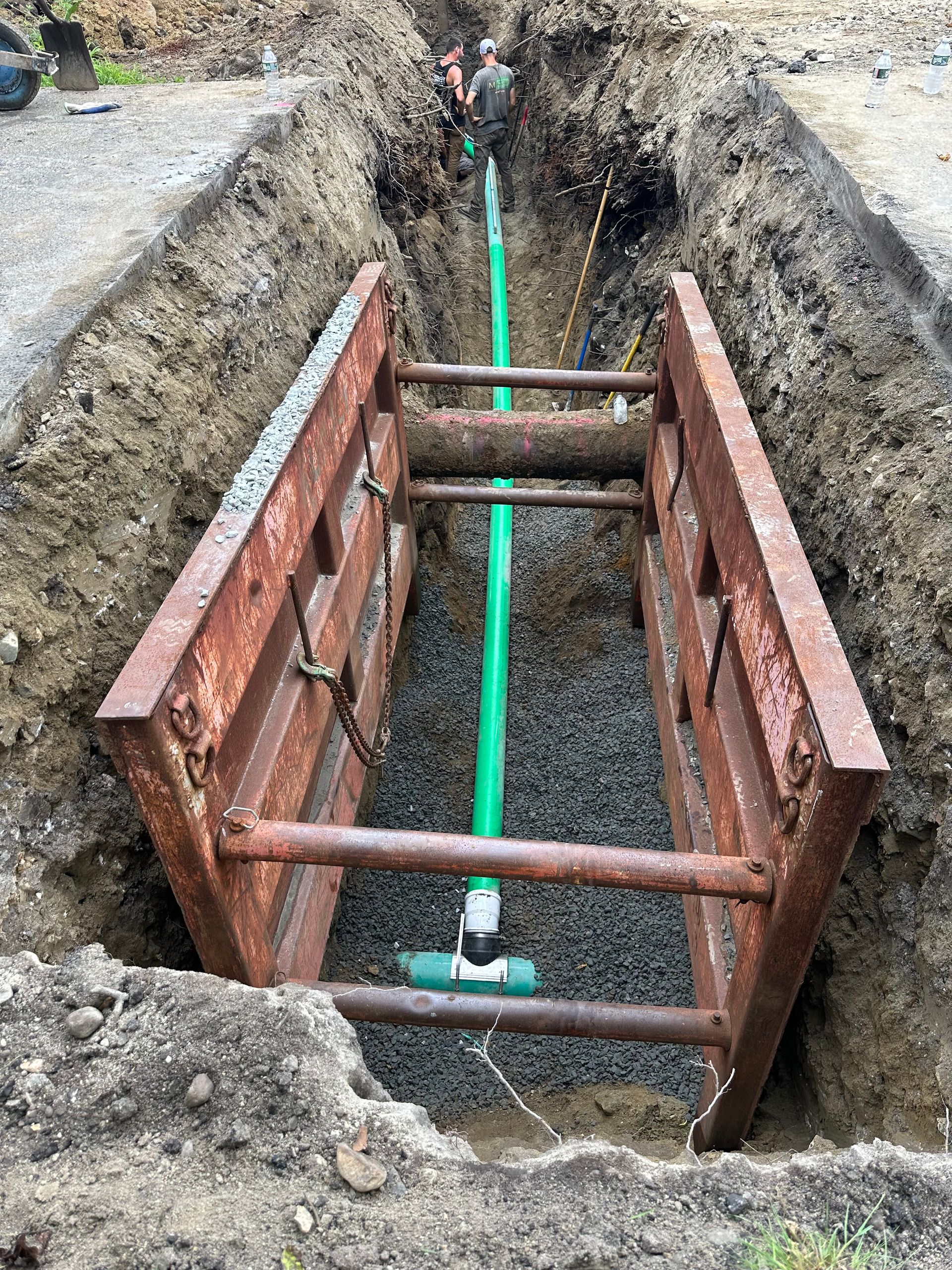 A green pipe is being installed in a trench.