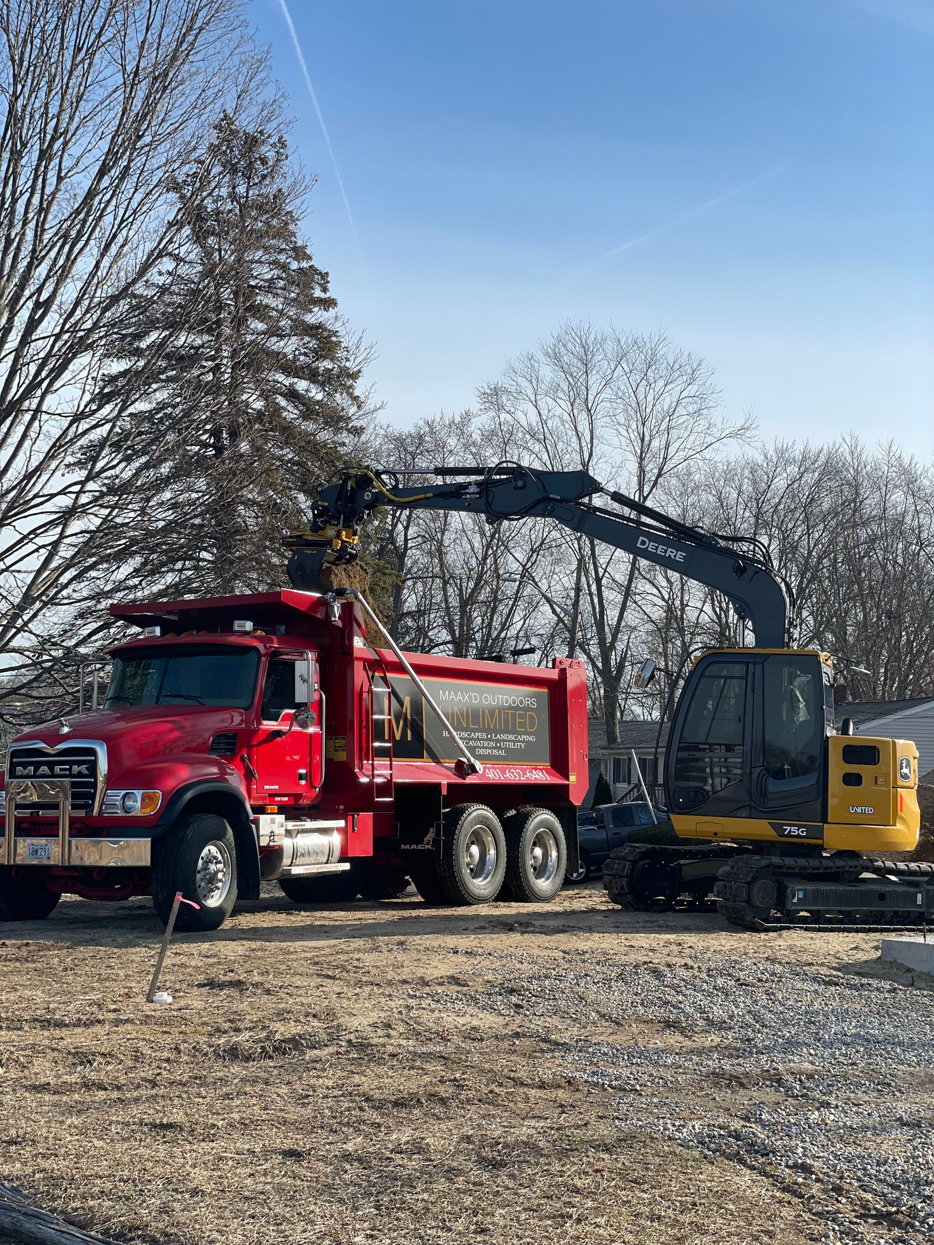 A red dump truck is parked next to a yellow excavator in a gravel lot.