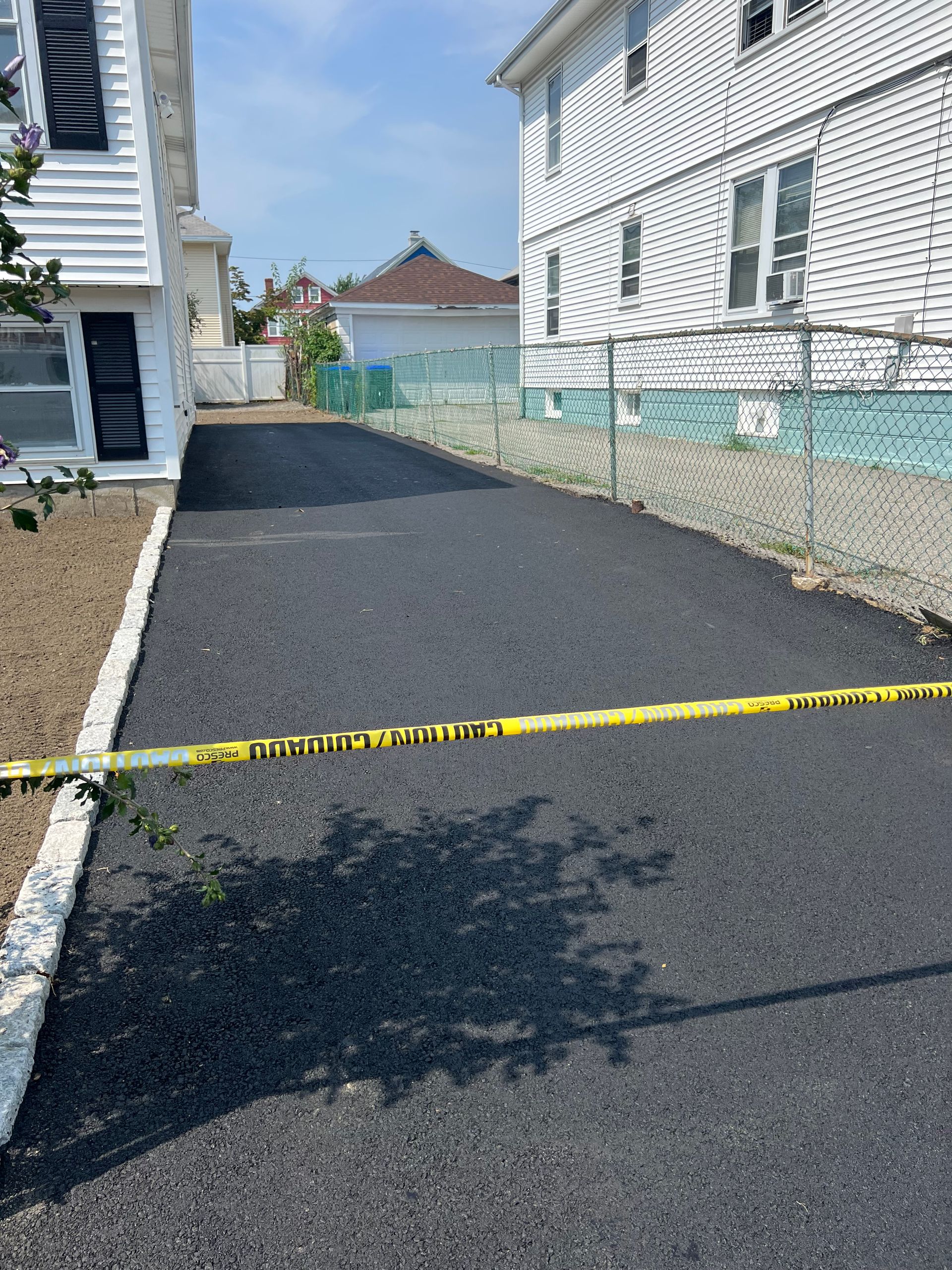 A driveway between two houses with a yellow caution tape.