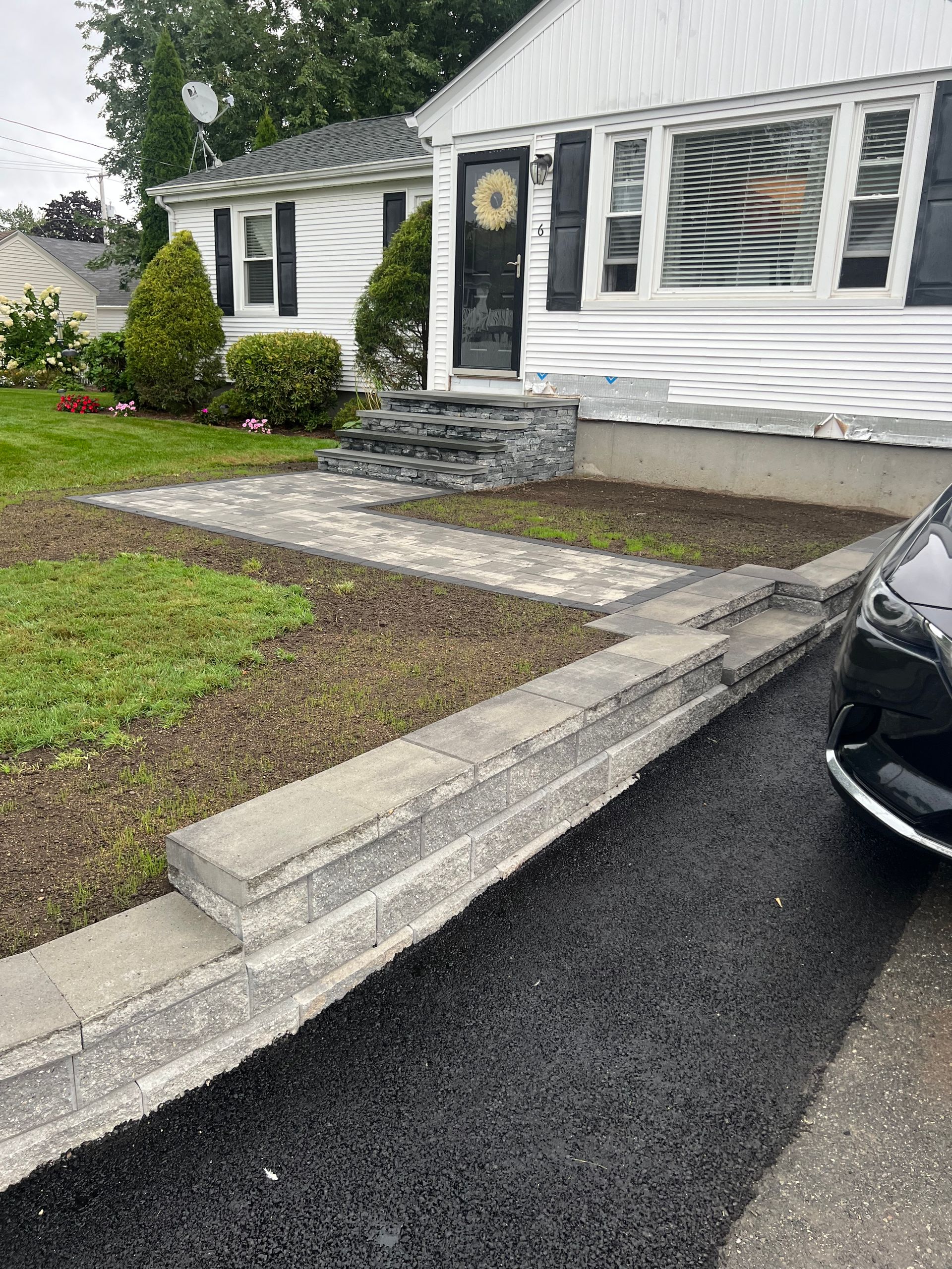 A black car is parked in front of a white house.