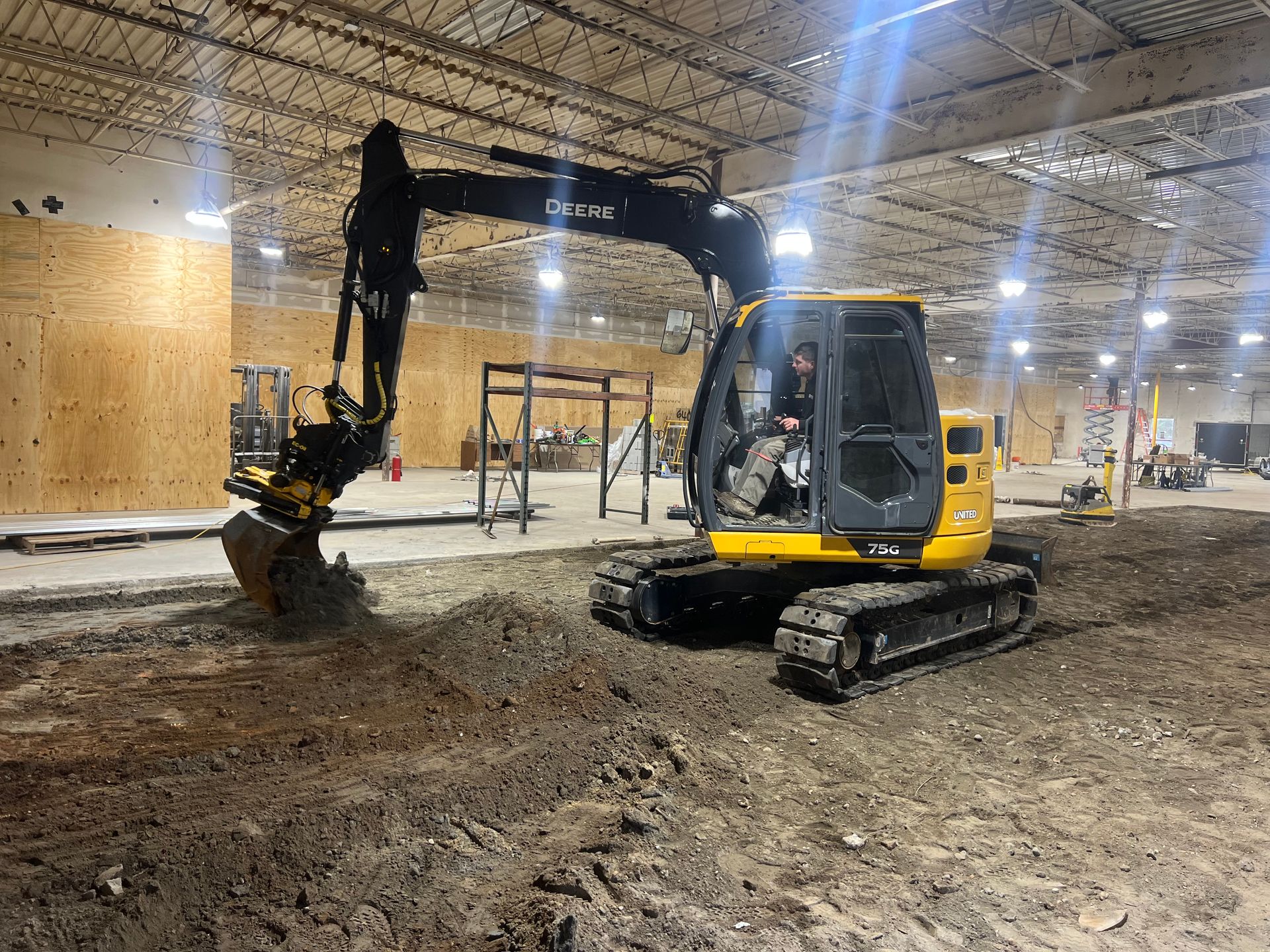 A yellow excavator is digging a hole in a large warehouse.