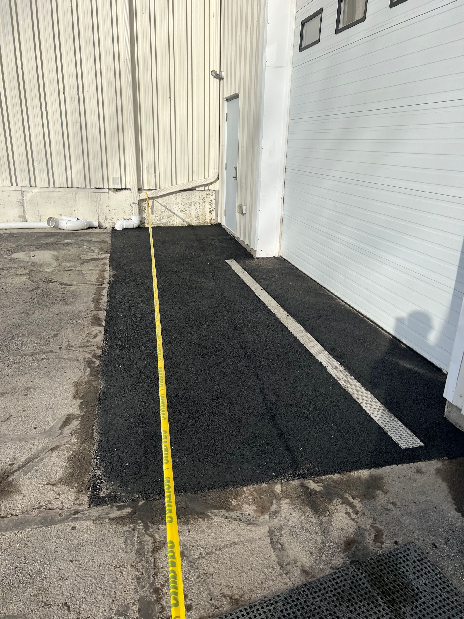 A yellow tape measure is laying on the ground next to a garage door.