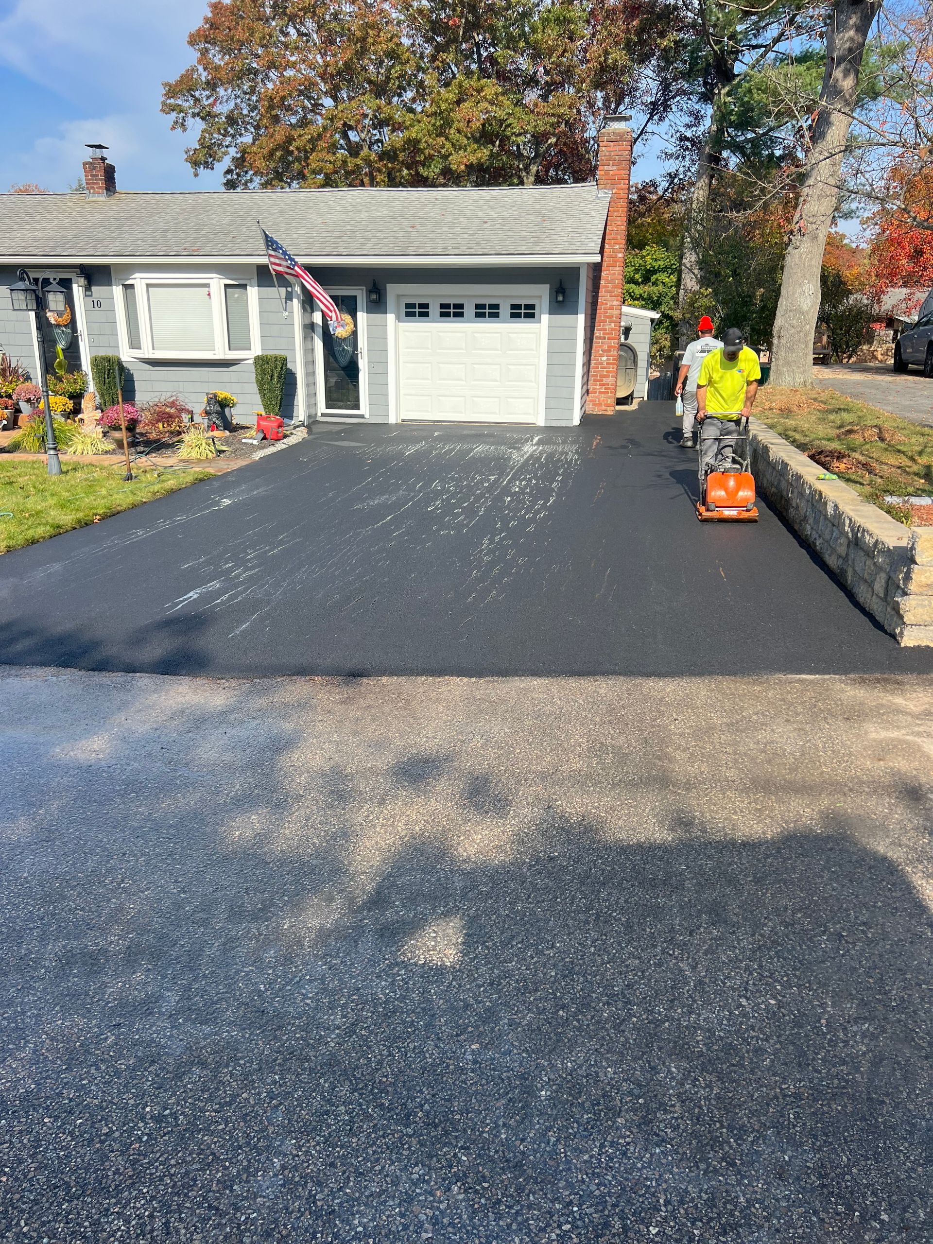 A man is using a lawn mower to cut a driveway in front of a house.