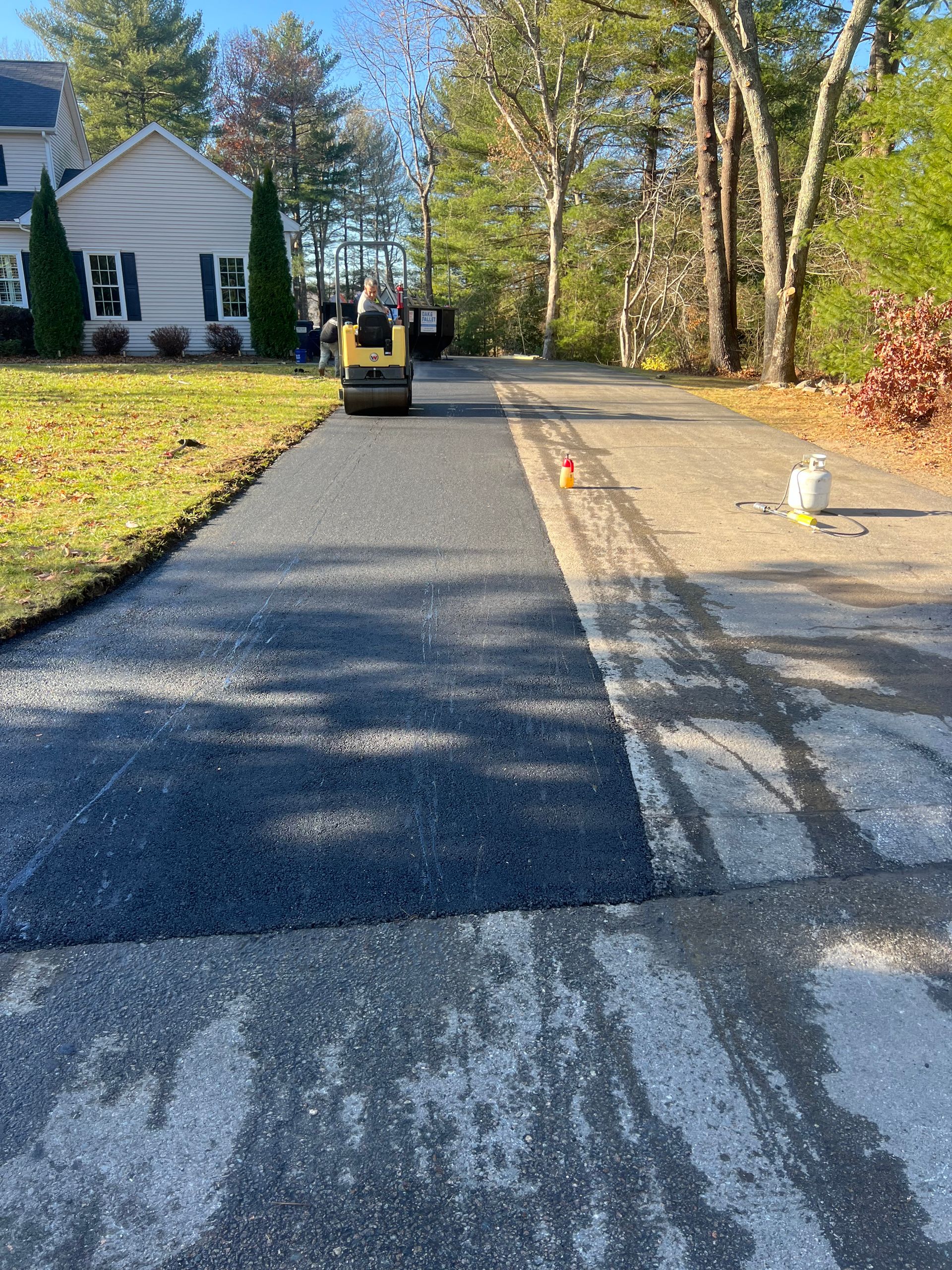 A machine is rolling asphalt on a driveway in front of a house.