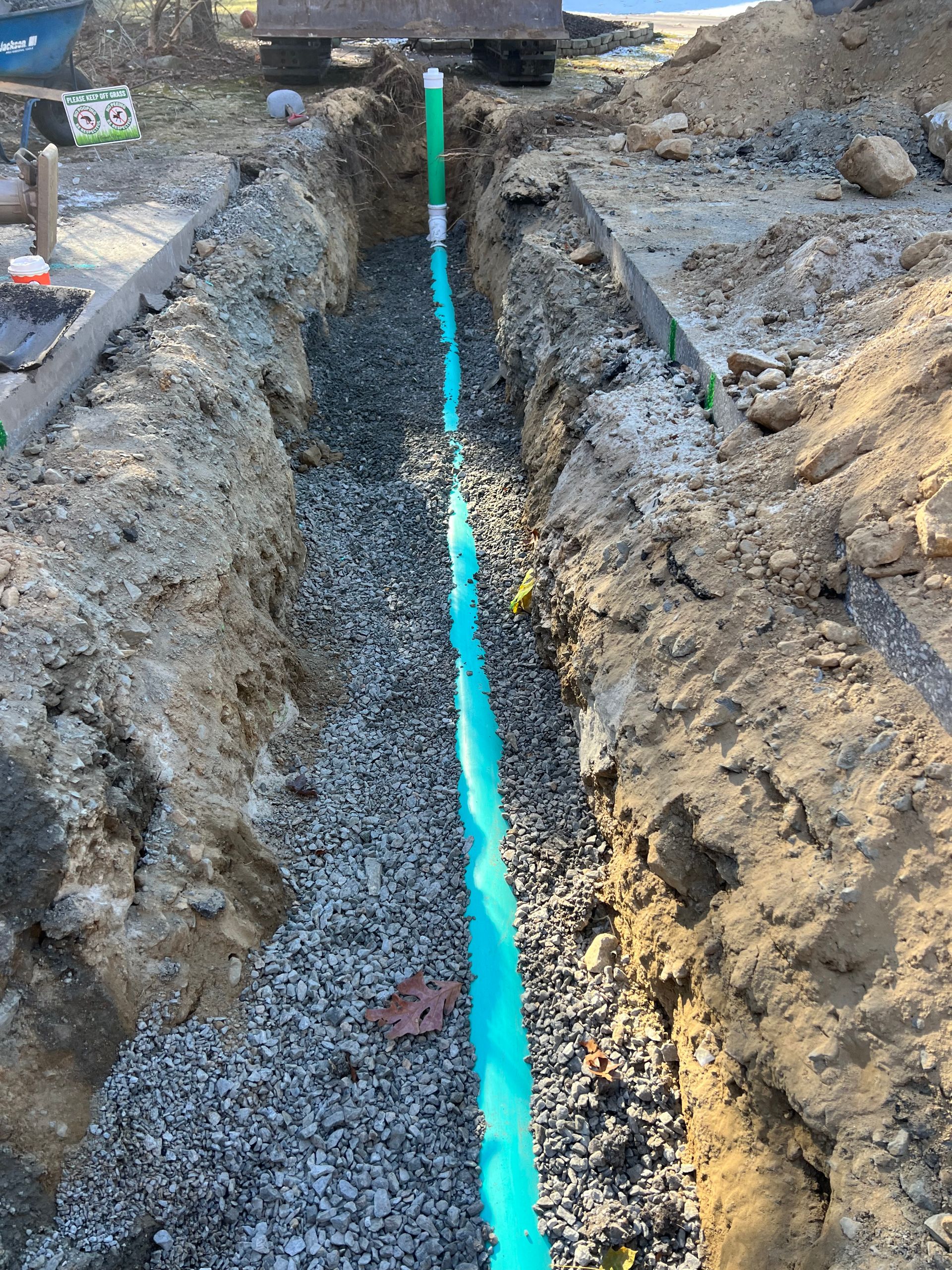 A blue pipe is being installed in a trench filled with gravel.