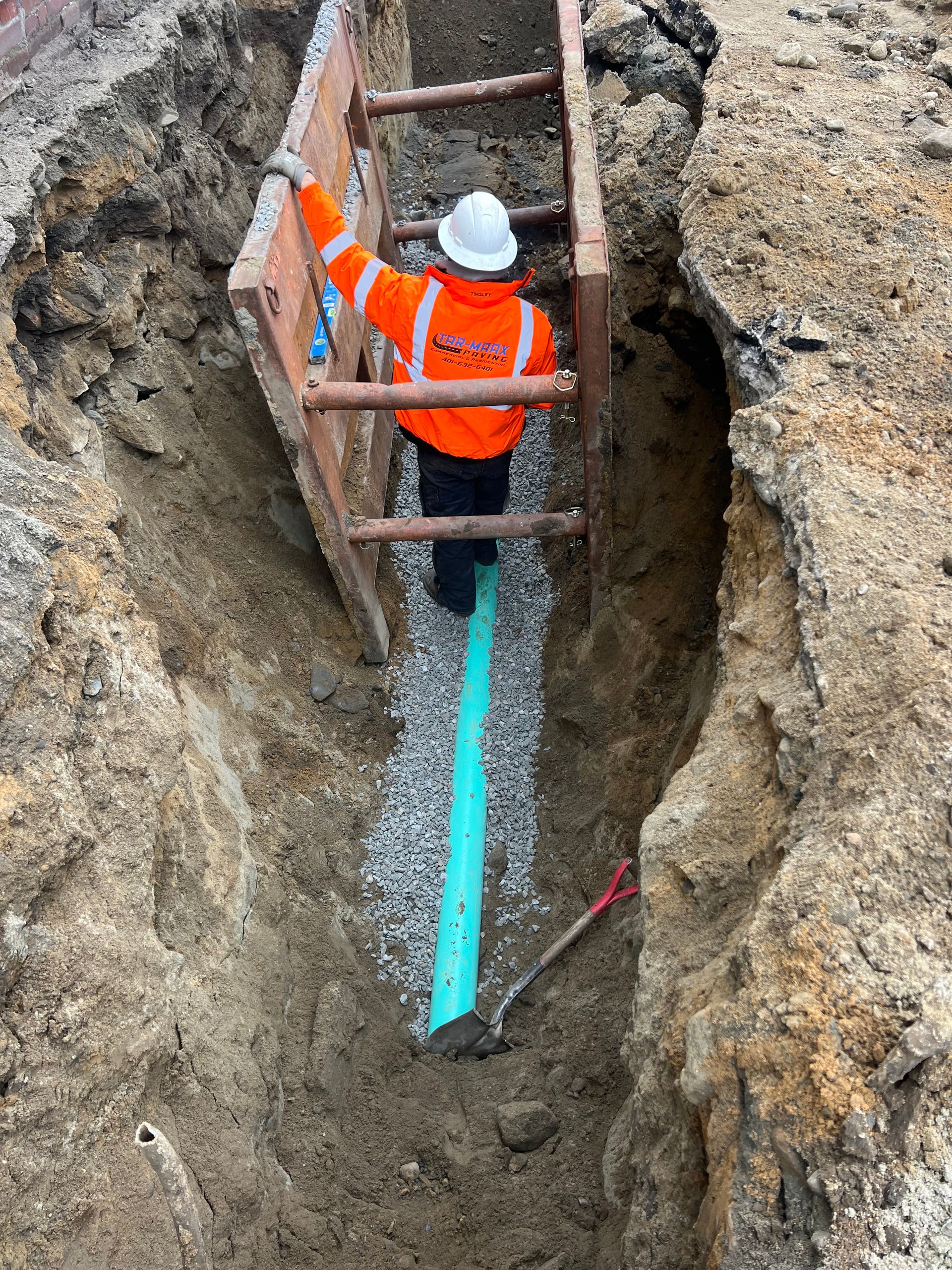 A man is standing in a trench next to a green pipe.