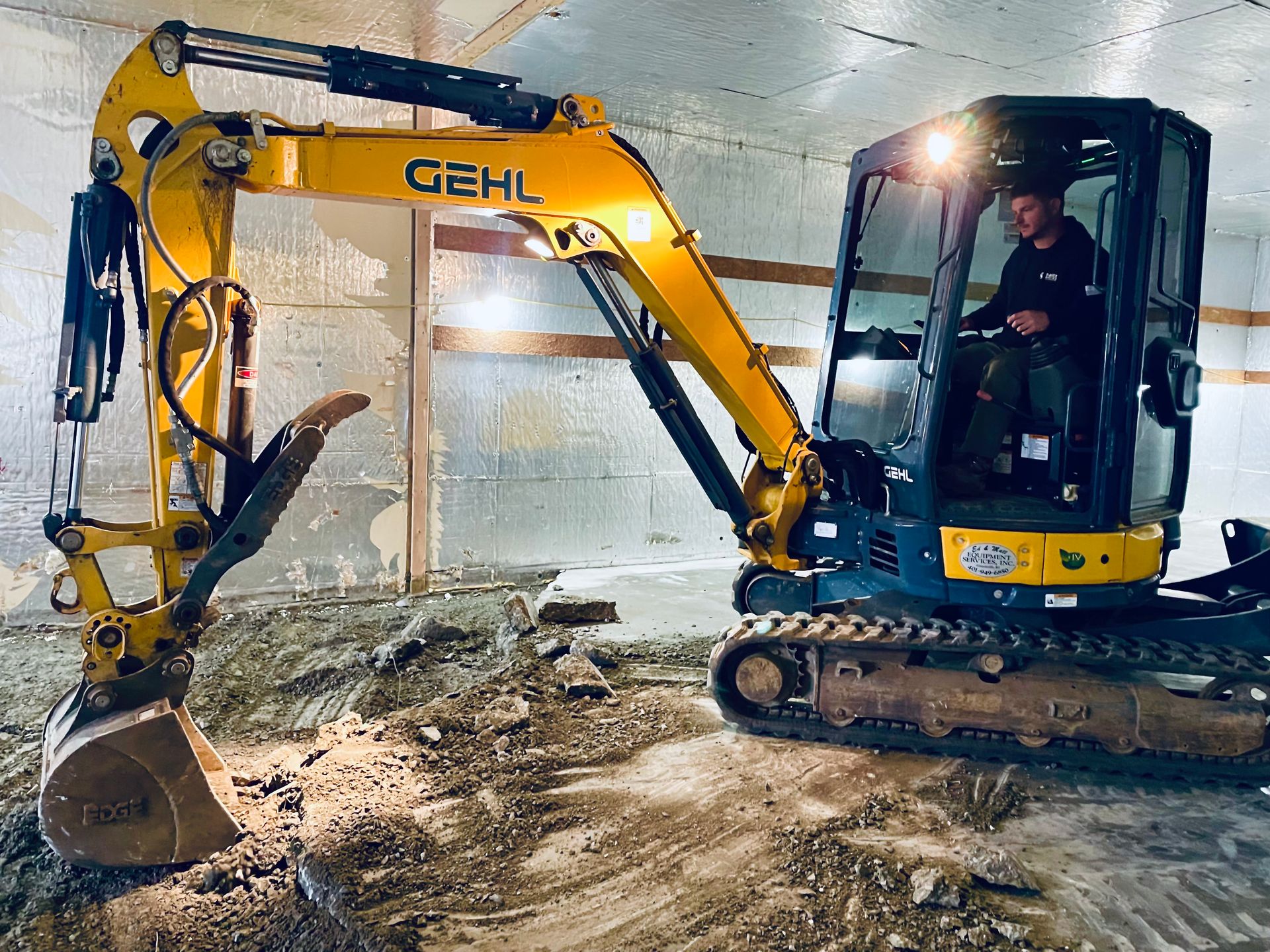 A man is driving a yellow excavator in a building.