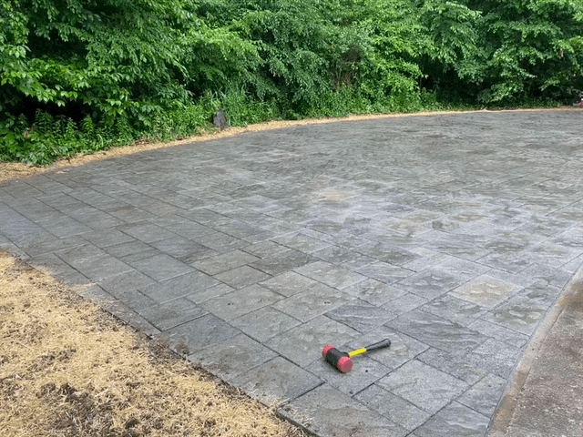 Concrete patio with a brick pattern, mallet, and green foliage in the background.