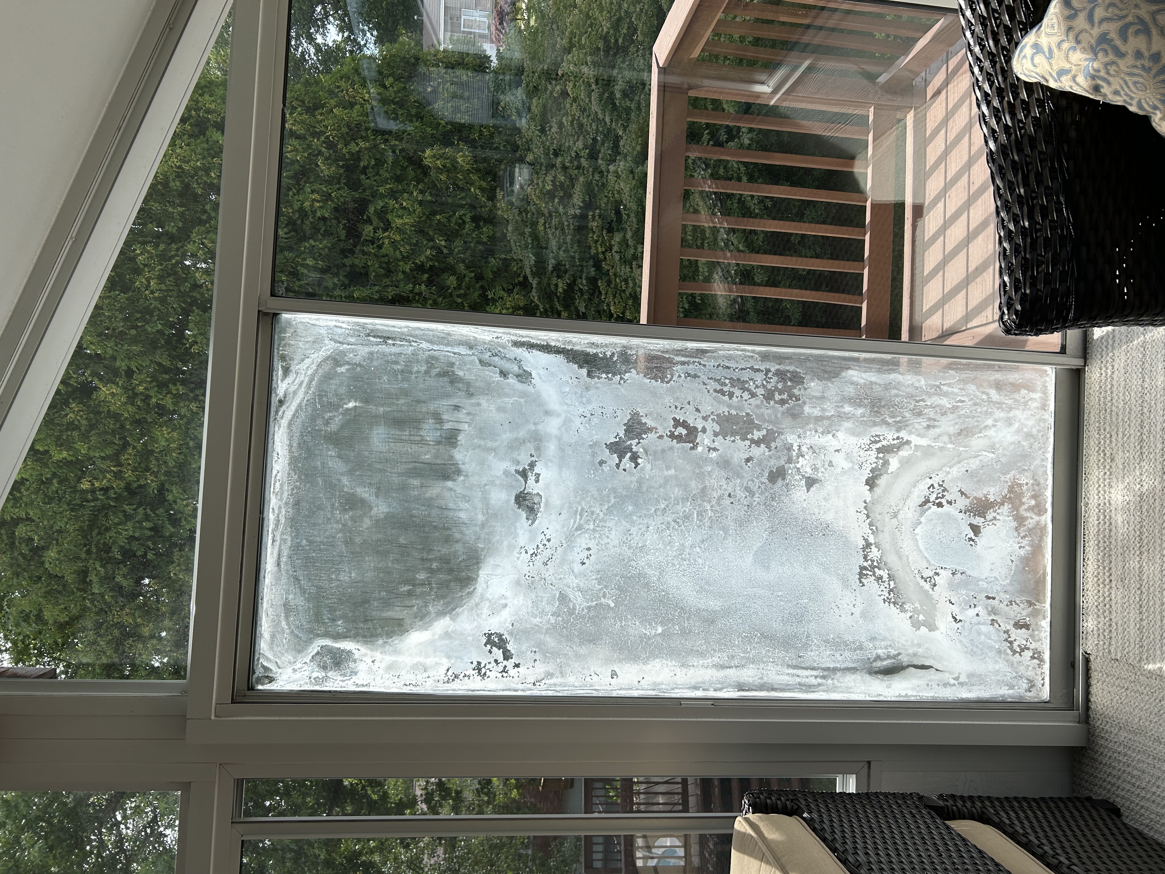 Hands wearing green gloves use a suction tool to install a glass window pane against a bright, cloudy sky background.