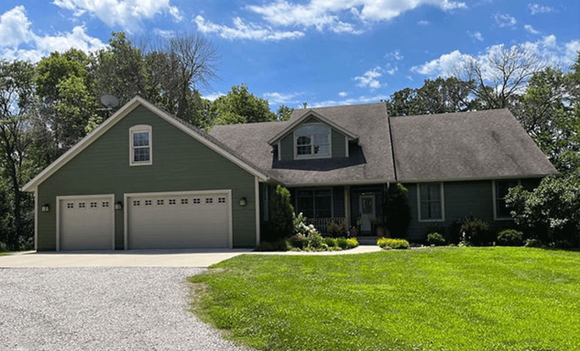 a large green house with a garage and a driveway in front of it .