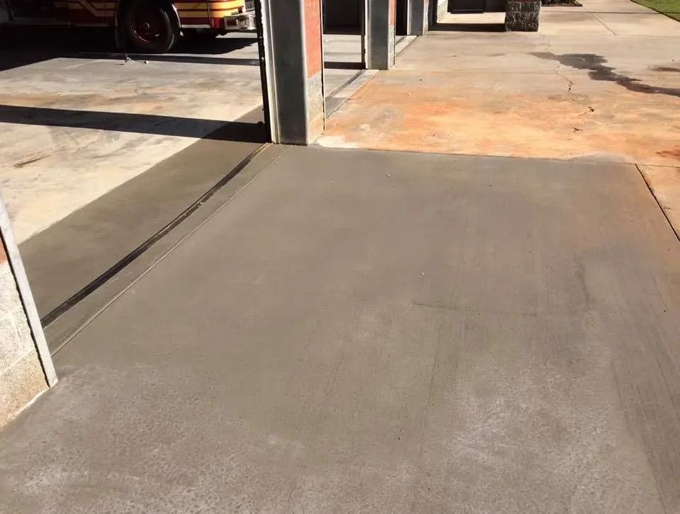 A freshly poured concrete ramp leads into a fire station bay with a drainage trench at the threshold.