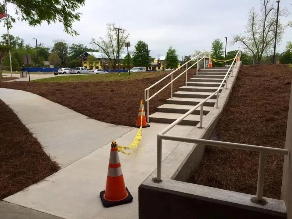 An outdoor concrete staircase with white railings, blocked by two orange traffic cones and yellow caution tape.