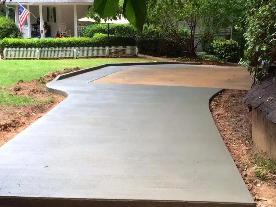 Freshly poured concrete patio section adjacent to an existing aged concrete driveway, set in a residential yard.