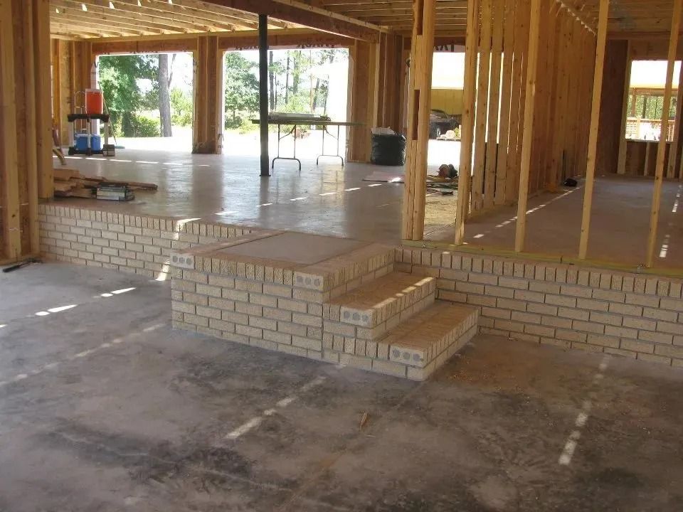 A partially constructed room with a raised wooden platform and brick stairs leading up to it, set in a wood-framed building.