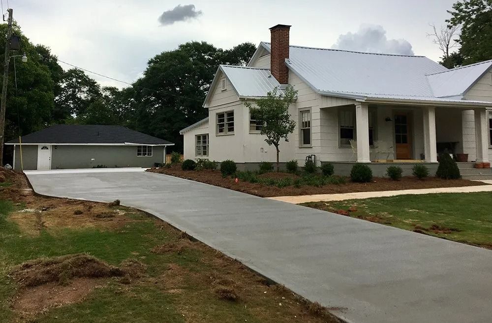 A white house with a metal roof and a detached garage connected by a newly poured, light-gray concrete driveway.