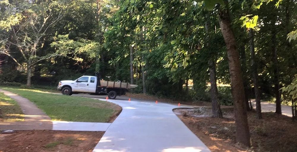 A white work truck parked on a newly paved concrete driveway surrounded by trees and a grassy lawn.