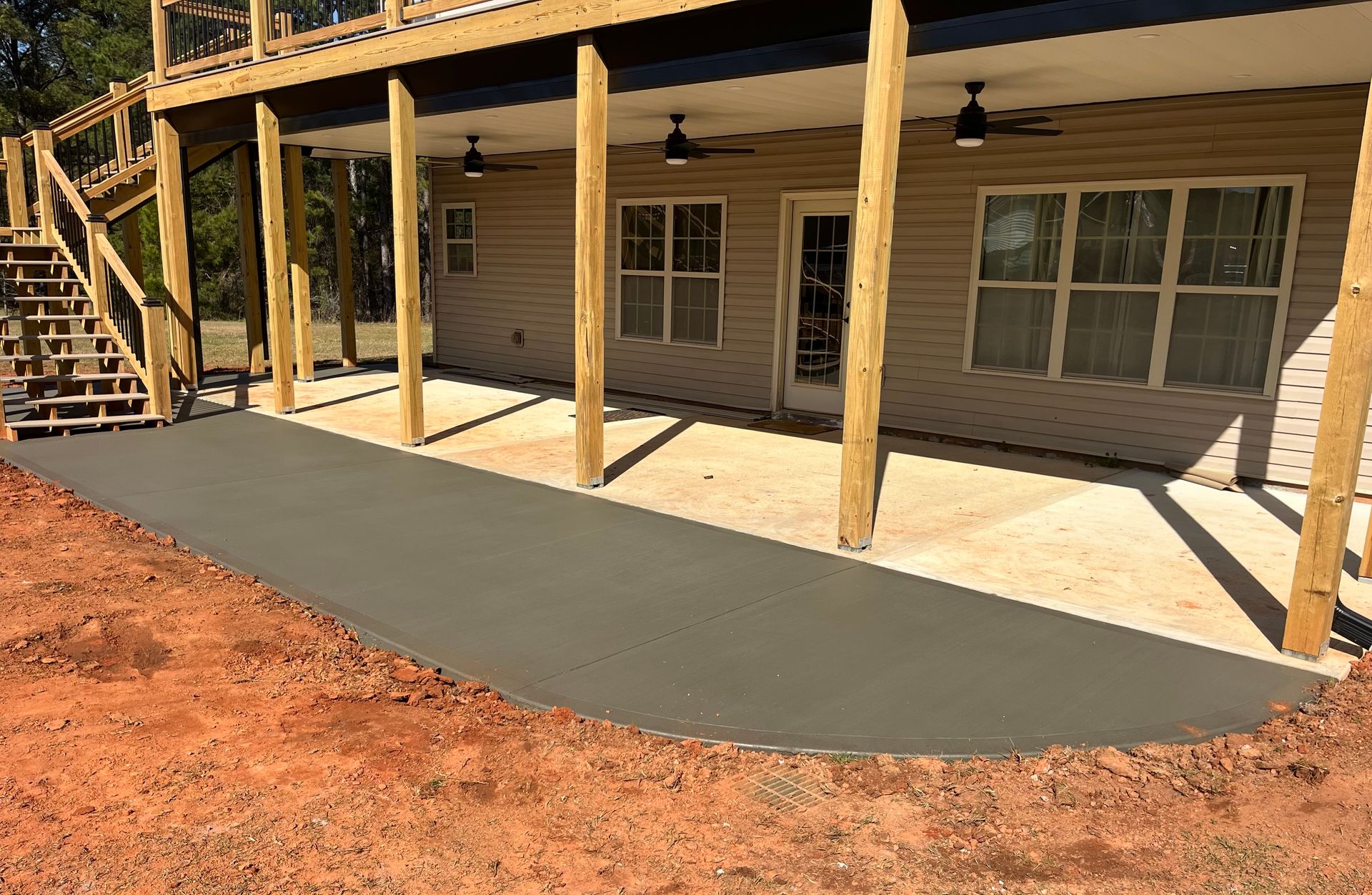 A freshly poured dark concrete patio extension adjacent to a covered porch with wooden support posts and stairs.