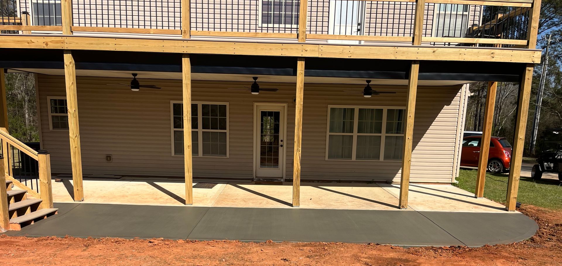 A neutral-toned house with a large wooden deck overhead, a covered concrete patio, ceiling fans, and wooden support posts.