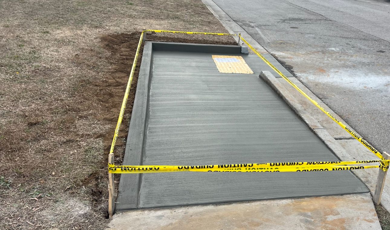A freshly poured concrete sidewalk landing with a yellow tactile warning surface, cordoned off by caution tape.