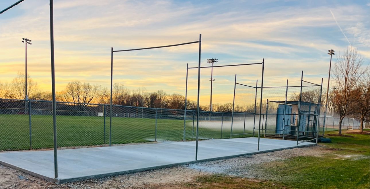 A paved sports area with pull-up bars and a nearby utility structure at sunset on a field.