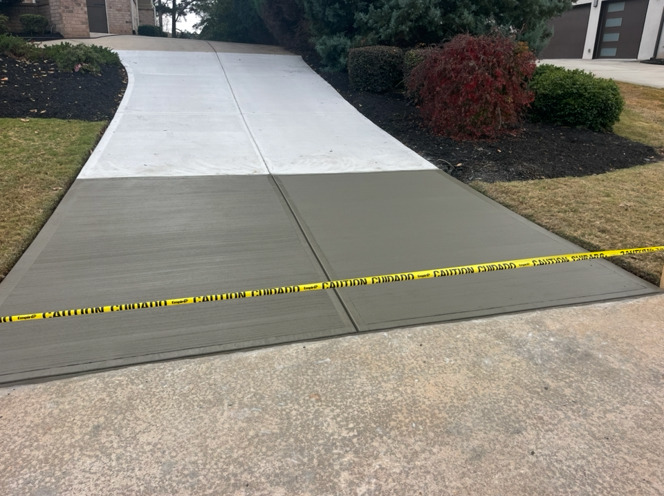 A residential driveway with a freshly poured, dark concrete section separated from lighter, older concrete by caution tape.