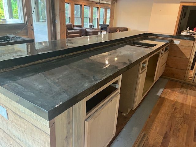 A kitchen island with unfinished light wood cabinetry and a dark, polished stone countertop under construction.