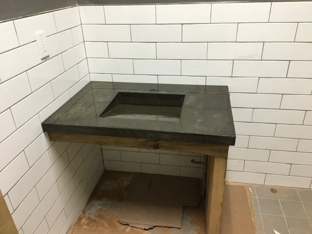 A dark concrete sink basin installed in a wooden vanity frame against white subway tile walls.