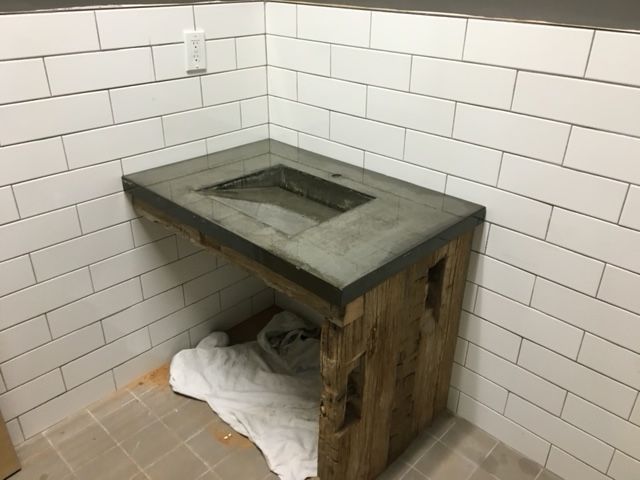A rustic concrete sink vanity sits in a corner against white subway tile walls.