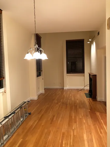 An empty living room with hardwood floors and a chandelier hanging from the ceiling
