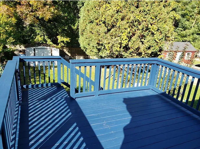 A blue deck with a white railing and trees in the background